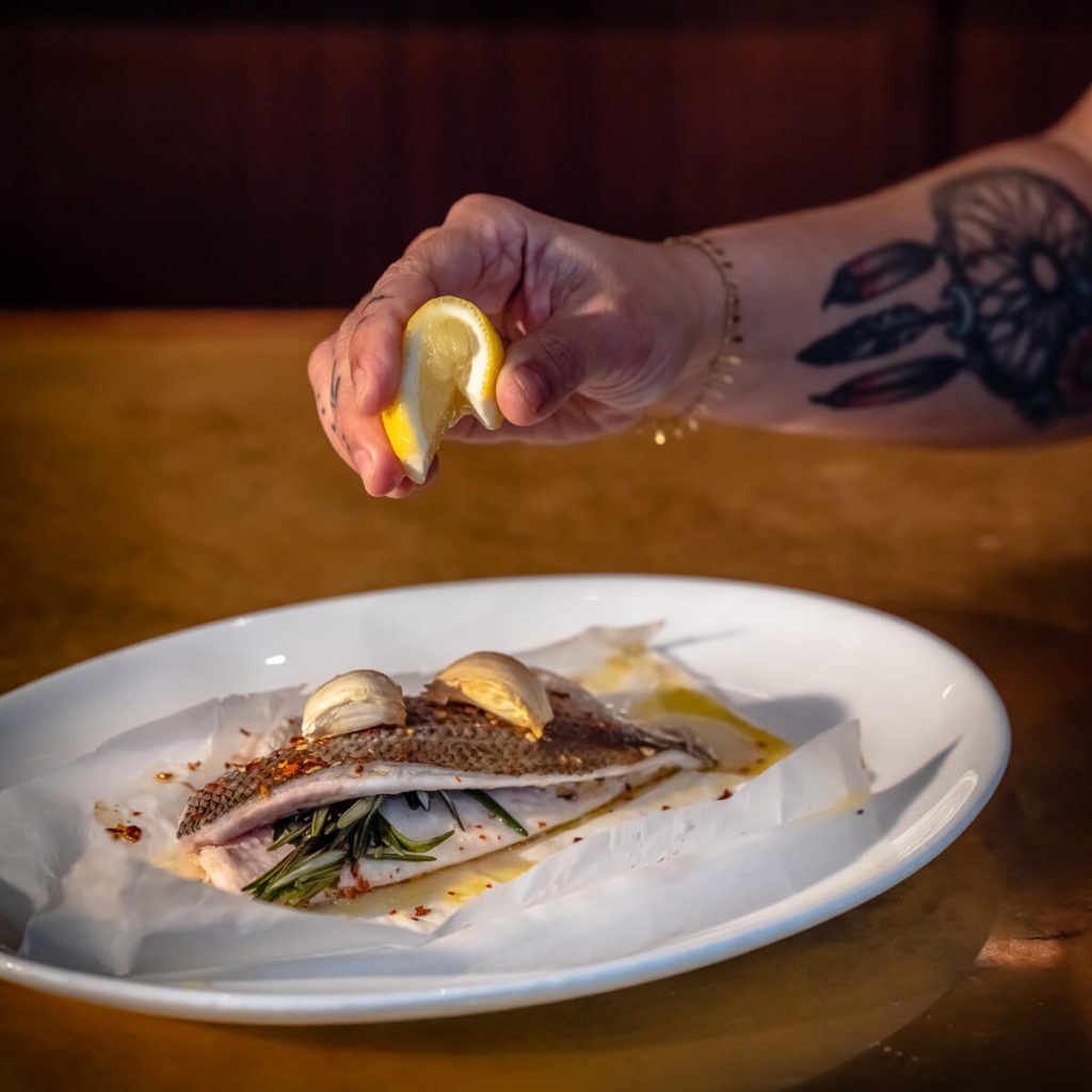 Hawksmoor Lunch Offerings 5 Close up of a marble bar counter with a selection of cocktails, sliders, sausage rolls, and Scotch eggs being served and enjoyed, with bartending tools and garnishes in the background