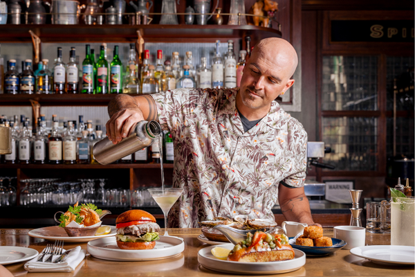A casually dressed bartender is pouring cocktails behind the bar