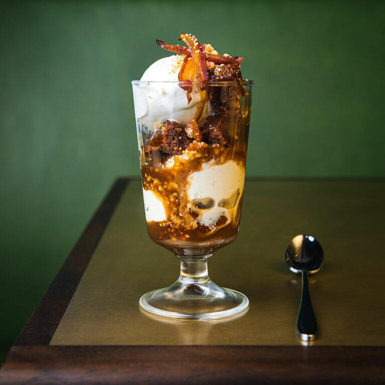 Hawksmoor Lunch Offerings 6 Cocktail bar interior with wood flooring, circular stools, art deco lighting, and a central marble counter set against shelves of spirits and a Beef & Liberty sign