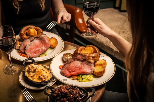 A wooden table with two plates of classic beef Sunday Roast with all the trimmings