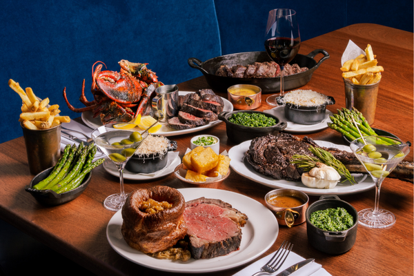 A wooden table laden with a variety of steaks, appetisers and sides