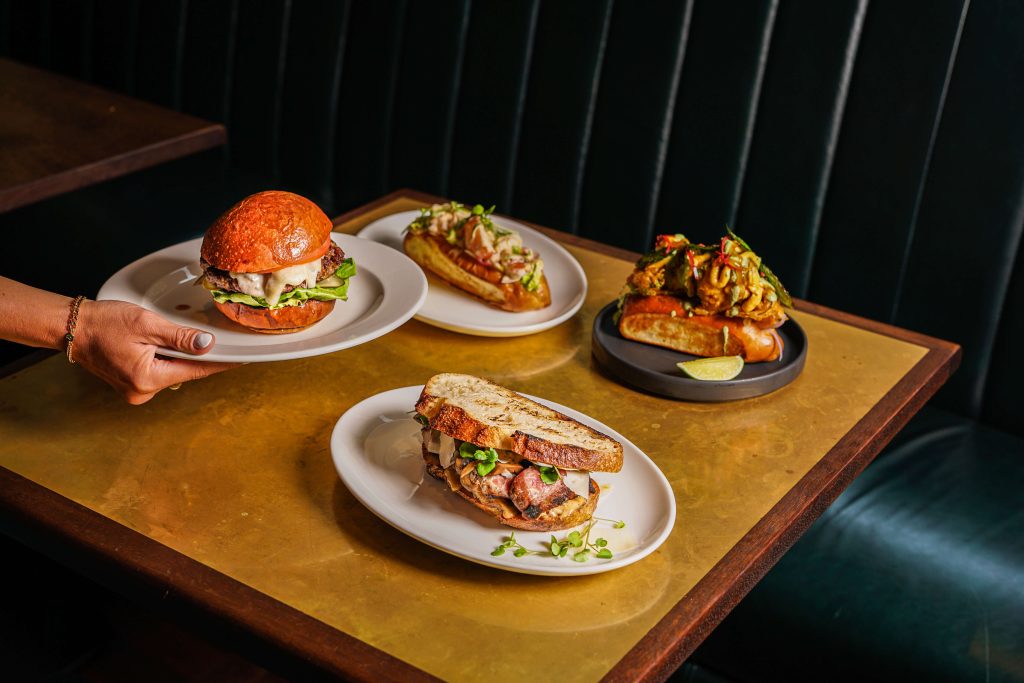 Hawksmoor Lunch Offerings 7 View of a cocktail bar with a prominent Beef & Liberty sign, dark panelled walls, brass fixtures, shelves filled with premium spirits, and a marble countertop